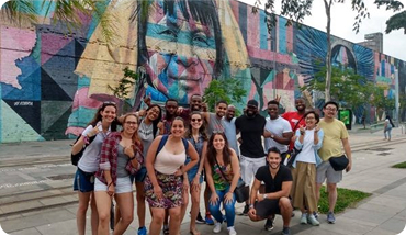 A group of people participating in the Boulevard Olympic and African Heritage tour by Free Walker Tours, posing in front of the famous graffiti "Etnias" by Kobra.